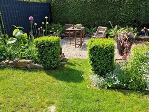 A garden with a wooden table and chairs, surrounded by hedges and plants.