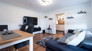 A modern living room with a dining table, sofa, TV, and kitchen in the background. - Apartment 'Ferienwohnung Sunny' with Mountain View and Wi-Fi (Schmallenberg)