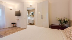Een slaapkamer met een bed, nachtkastje, televisie aan de muur, kledingkast, en een badkamer zichtbaar door een open deur.