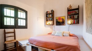 A bedroom with a bed, a chair, a bookshelf, and a window.