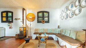 A cozy living room with a wooden sofa, a small table, wicker stools, and decorative plates on the wall.