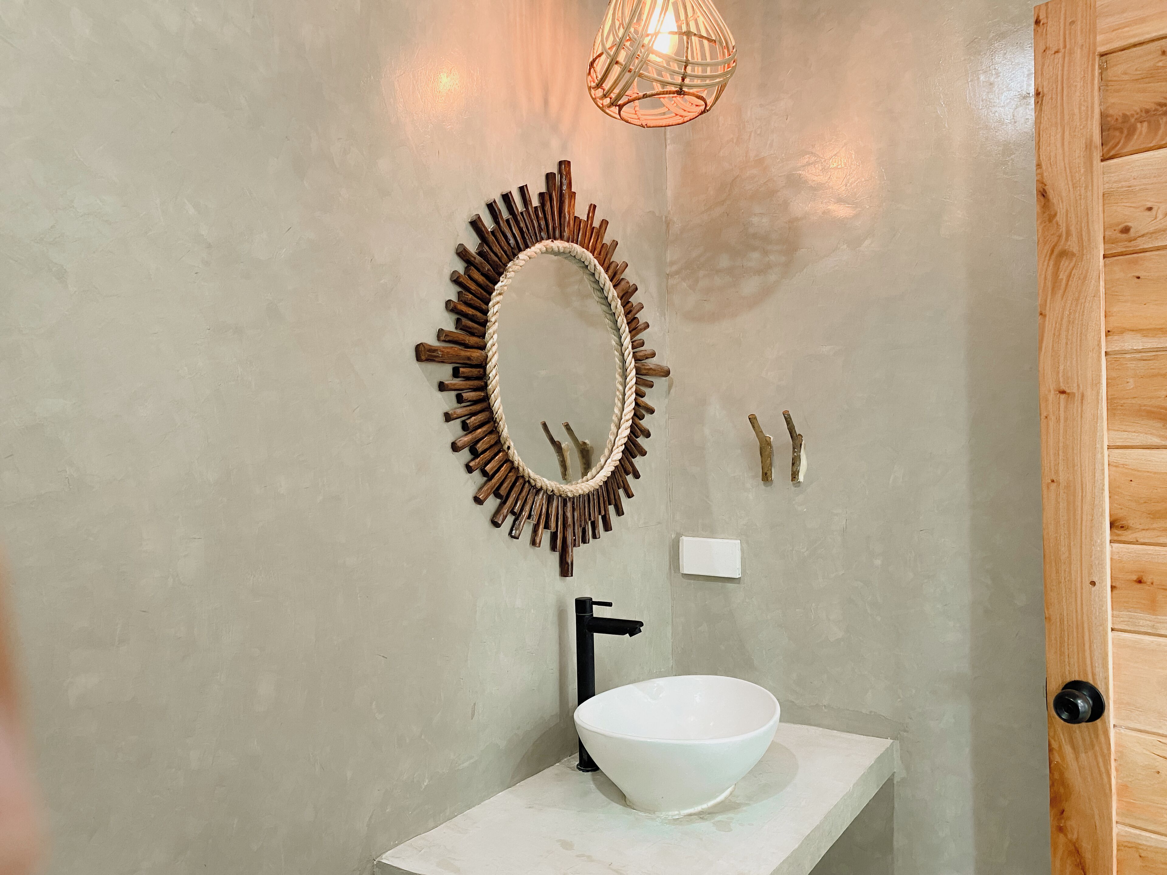 A bathroom with a round mirror, wooden wall decor, a white sink, and a wooden door.