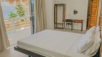 Un dormitorio con cama, escritorio, silla y un espejo grande. Se ve el exterior a través de una puerta de cristal.