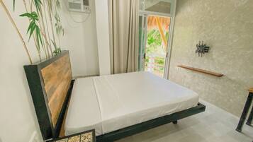 A bedroom with a bed, a wall-mounted air conditioner, a window with curtains, a small shelf, and a tiled floor.