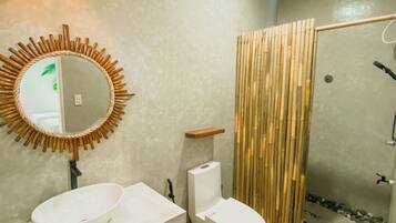 A bathroom with a round mirror, two sinks, a toilet, and a shower area with bamboo panels.