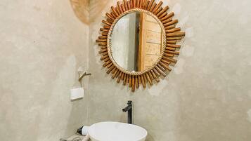 Une salle de bain avec un miroir rond encadré de bois, un lavabo blanc et un porte-serviettes.