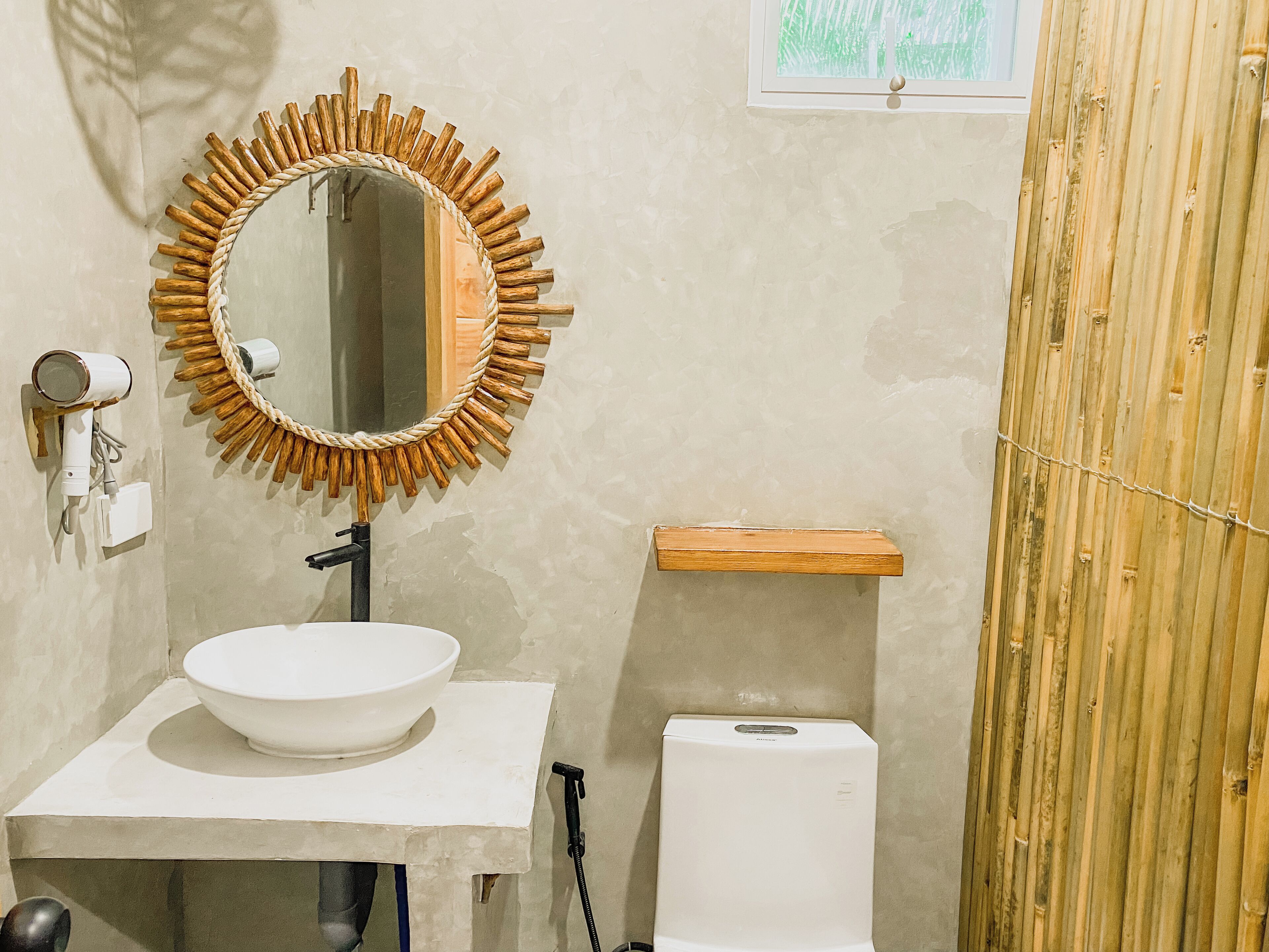 A bathroom with a round mirror, a white sink, a toilet, and a wooden shelf.