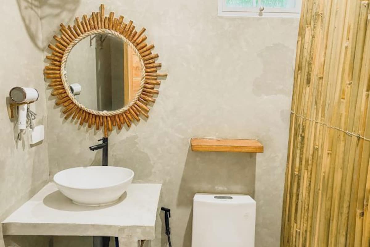 A bathroom with a round mirror, a white sink, a toilet, and a bamboo wall.