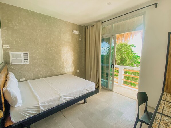 Habitación de hotel con cama, una silla, balcón con vistas a zonas verdes y un equipo de aire acondicionado en la pared.