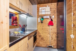 Una cocina compacta con armarios de madera, cafetera, lavamanos y escoba.