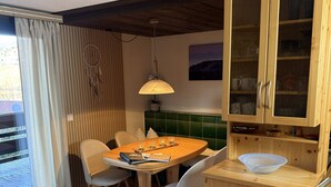 A dining area with a wooden table, chairs, a green cushioned bench, and a wooden cabinet with glass doors. - Holiday Apartment Herzogenhorn with Mountain View, Private Terrace and Wi-Fi (Bernau im Schwarzwald)