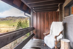Un porche de madera con un banco y una silla, con vistas a un paisaje rural.