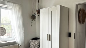 Une chambre avec une grande armoire, un lit, une fenêtre avec des rideaux et une plante suspendue.