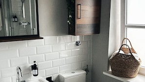 Une salle de bain avec un lavabo blanc, des toilettes, un miroir, une douche et une fenêtre.