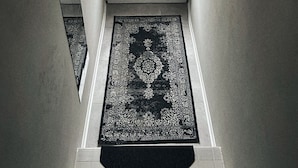 Un couloir avec une porte, un tapis et un miroir.