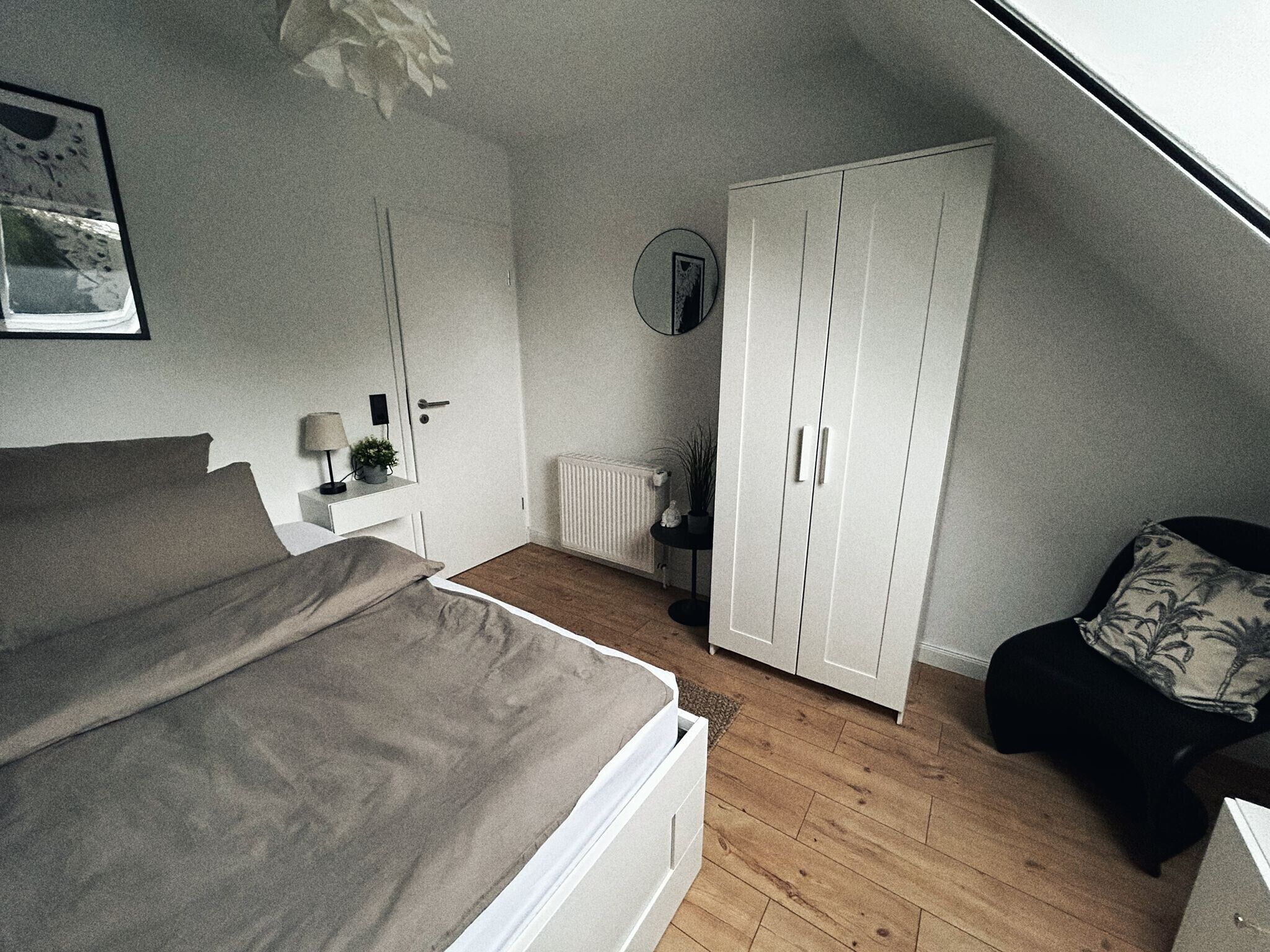 Une chambre à coucher comprenant un lit, une armoire, un radiateur, une petite table avec une lampe et une plante en pot.