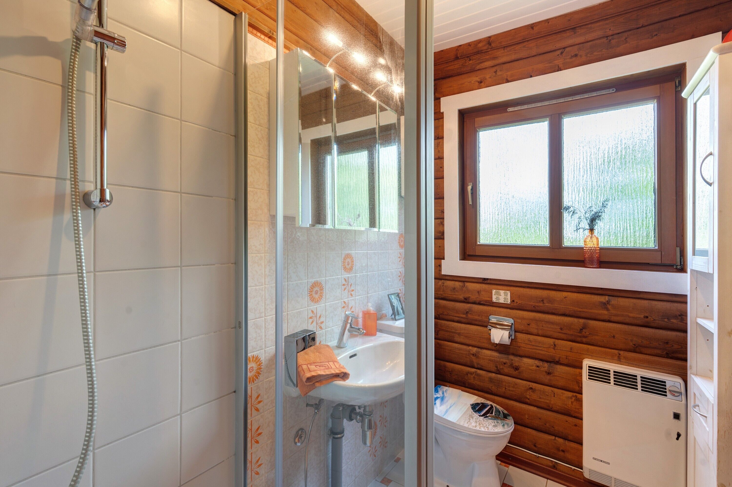 Une salle de bain avec douche, lavabo et toilettes, des murs en bois et une fenêtre.