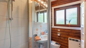 Une salle de bain avec douche, lavabo et toilettes, des murs en bois et une fenêtre.