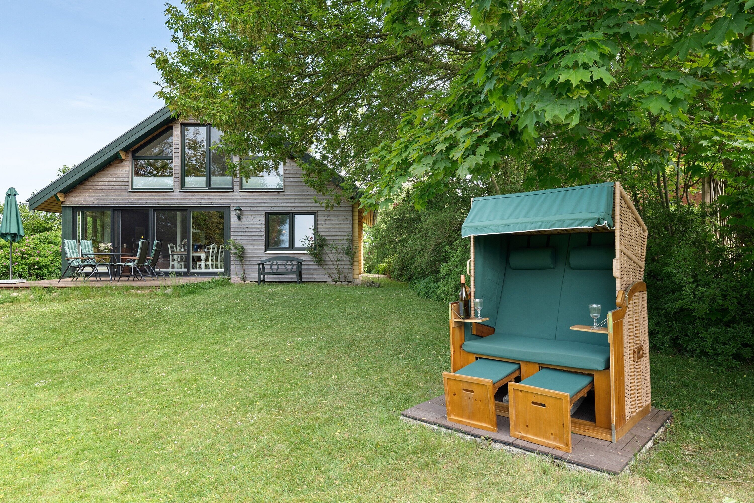 A modern house with a deck, a green outdoor seating area, and a well-maintained lawn.