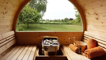 A sauna room with a wooden bench, a bucket of hot stones, and towels.