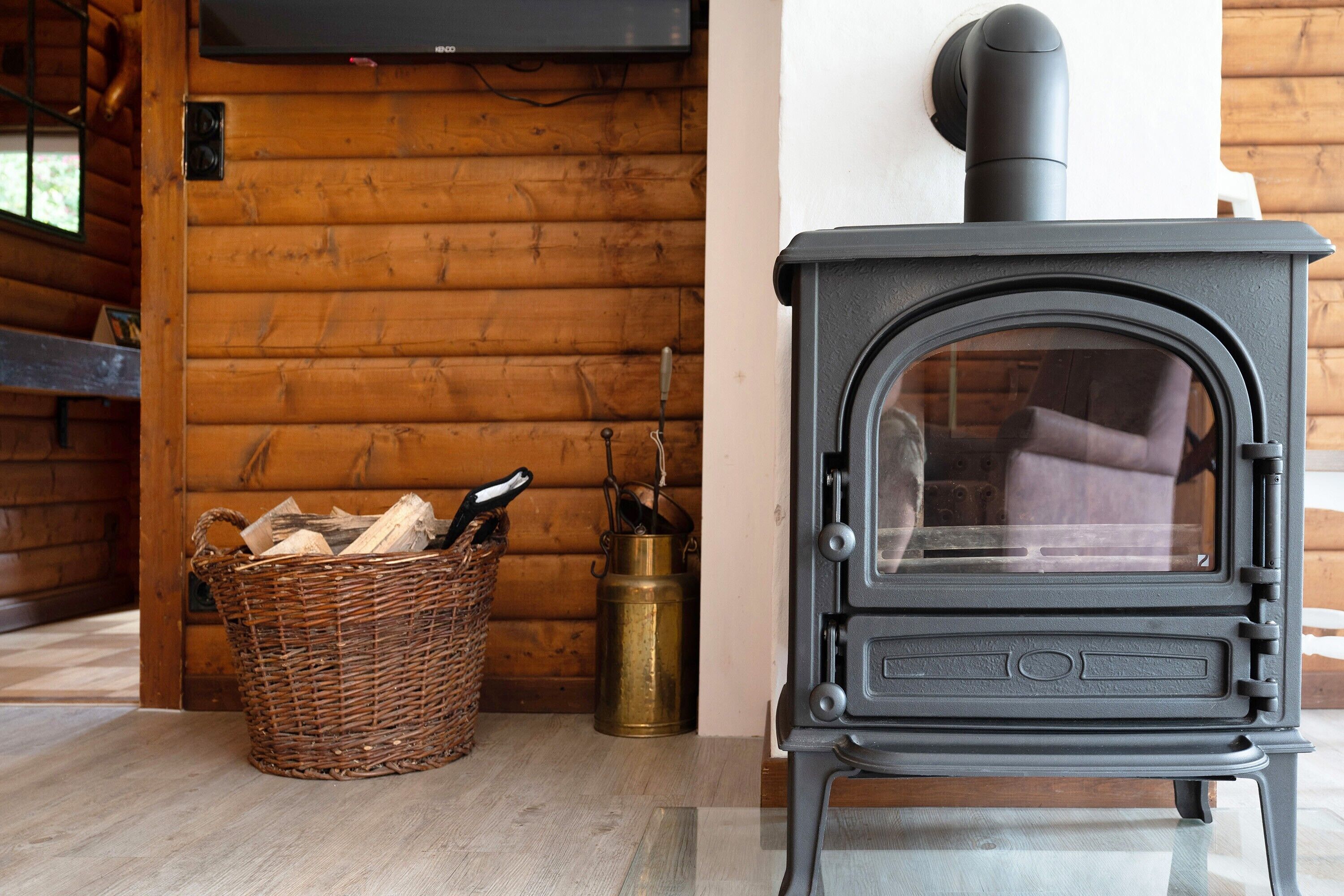 A wooden interior with a black wood stove, a wicker basket with firewood, and a brass lantern.