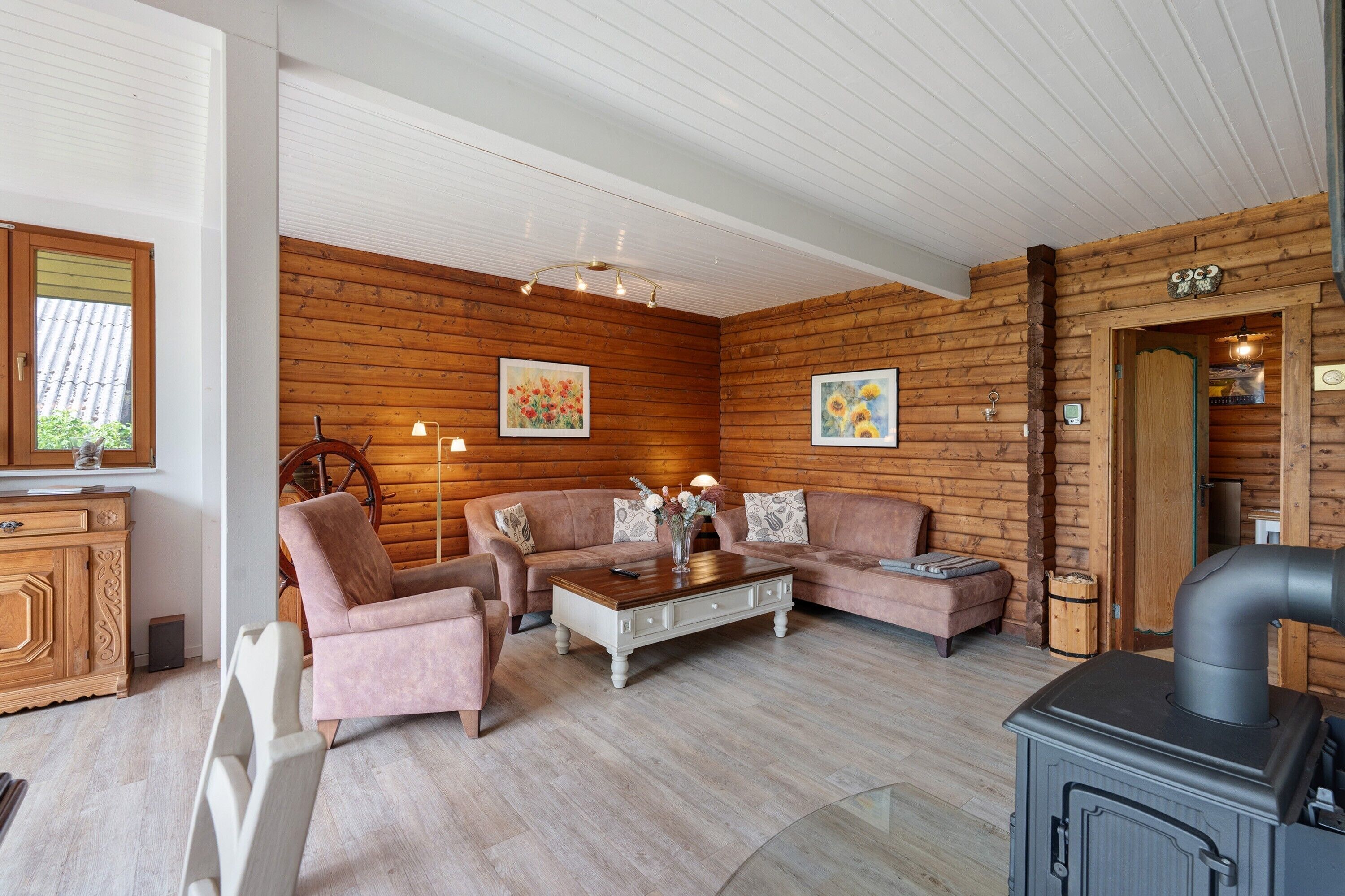 Interieur van een blokhut met een houten wand, een zithoek, een salontafel, een open haard en een houten kast.
