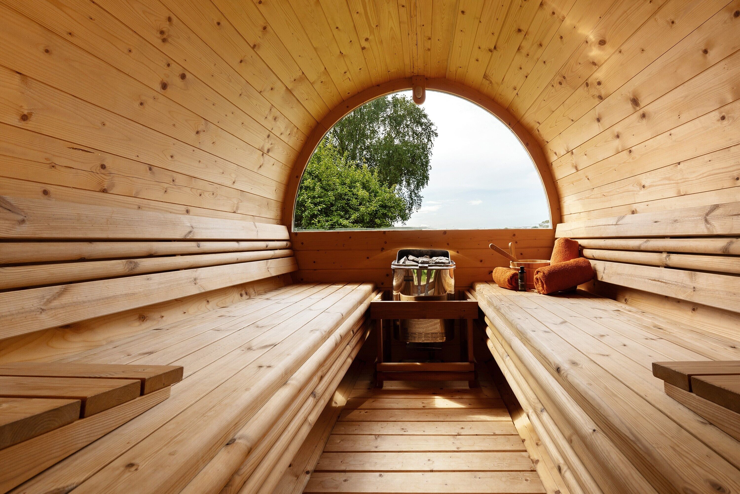 A sauna with wooden benches and a bench table with towels and bottles.