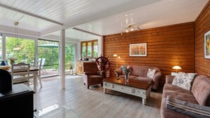 A spacious living room with wooden walls, a wooden coffee table, two sofas, and a dining area with a table and chairs.