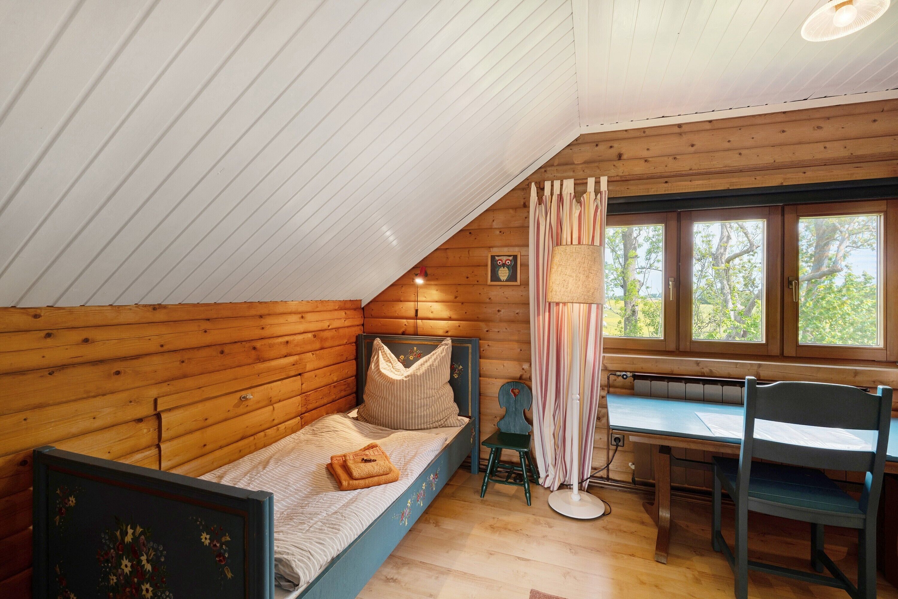 A bedroom with a sloped ceiling, a wooden bed, a desk, and a chair.