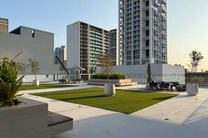 A rooftop garden with seating areas, a small pool, and modern buildings in the background. - Vogue | Binghatti Corner JVC near Circle Mall (Dubai)
