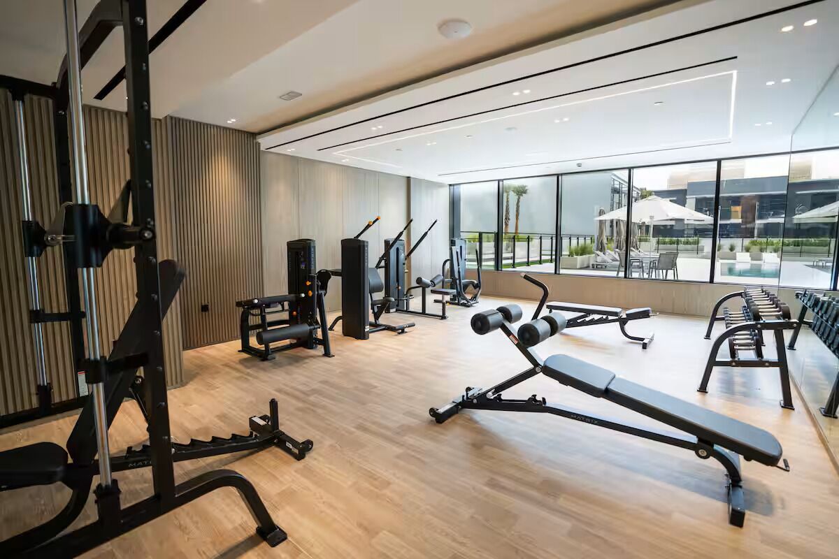 A modern gym with various exercise equipment, large windows, and a view of the outdoors.