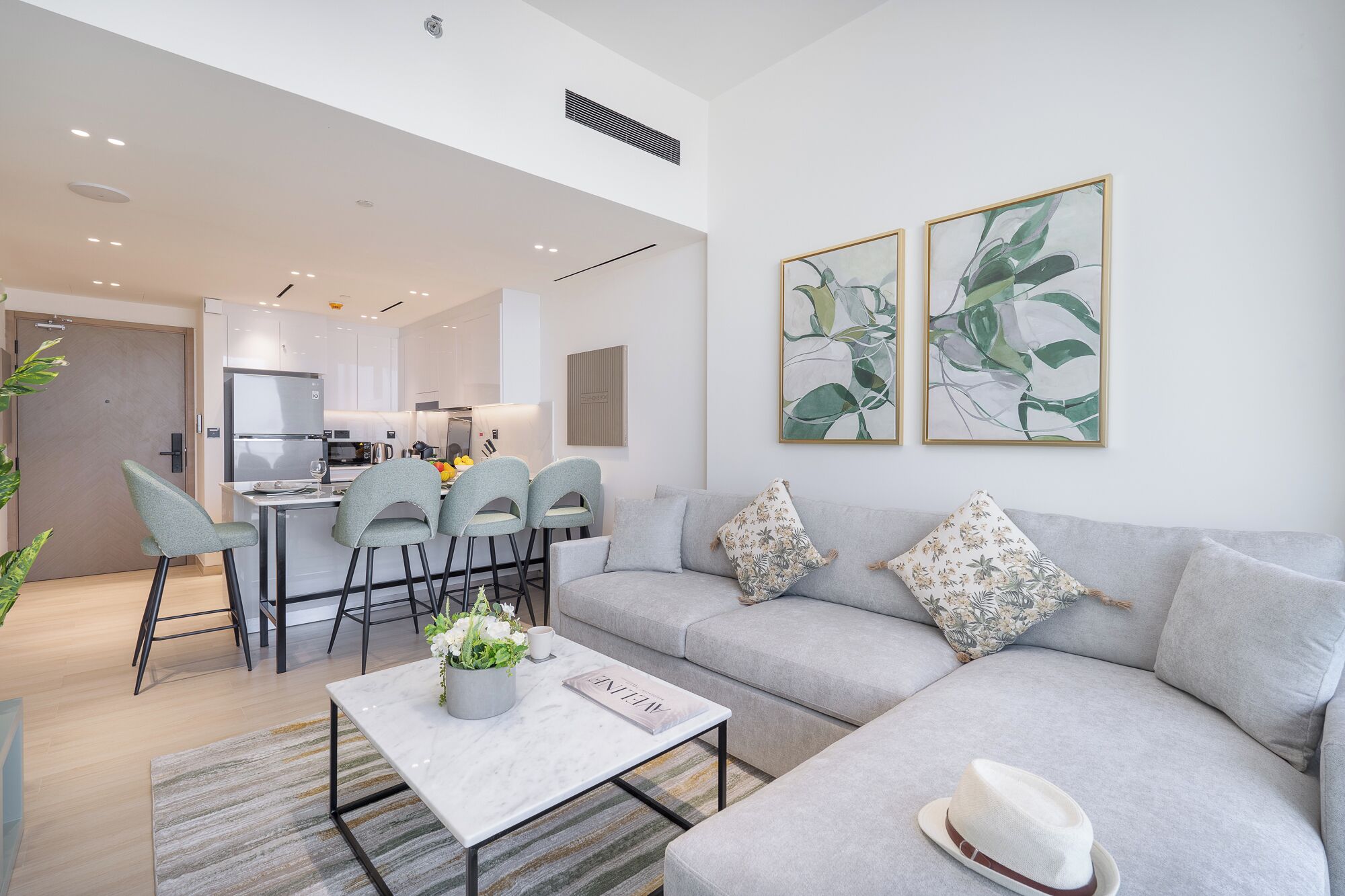 Un salon moderne avec un canapé gris, une table basse et un coin repas comprenant des chaises, et une cuisine en arrière-plan.