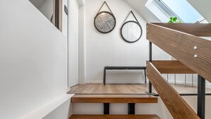 Een moderne trap met houten treden en metalen leuningen, die uitkomt op een plateau met een bankje.
