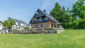 Een huis met twee verdiepingen, een stenen steunmuur, een balkon en een verzorgd gazon.