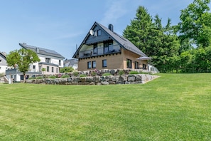 A two-story house with a stone retaining wall, a balcony, and a well-maintained lawn.