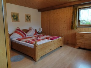 A wooden-paneled room with a bed, a dresser, and two wall-mounted paintings.