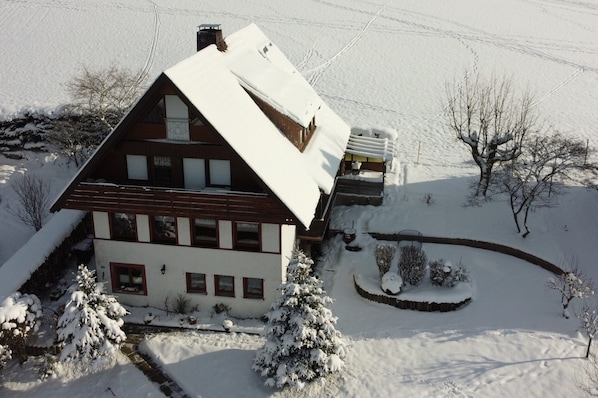 A two-story house with a snow-covered roof and a small garden area.