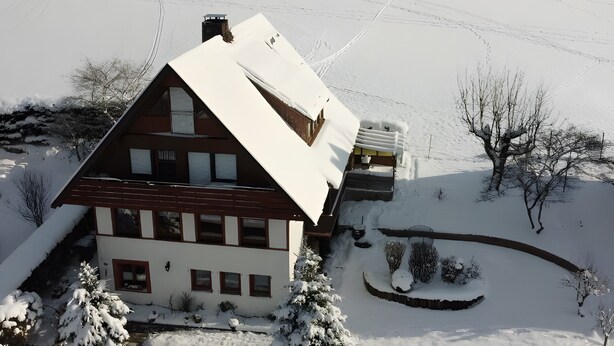 Une maison à deux étages, dotée d’un toit en pente, entourée d’un paysage enneigé et d’arbres.