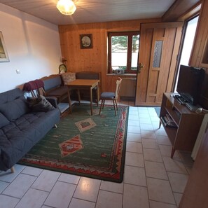 Un salon chaleureux avec un canapé, une table à manger en bois, un meuble pour la télévision et un tapis à motifs.