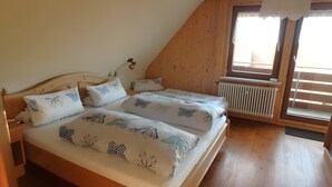 Une chambre avec un plafond en pente, des murs en bois, un lit avec une literie à motifs, une table de chevet et une fenêtre avec des stores.