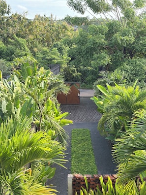 A garden with a paved pathway, lush greenery, and a wooden gate. - TWINSEAS VILLA (Ungasan)