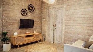 Een woonkamer met een houten wand, een televisie boven een houten kast, een rond geweven vloerkleed en een bank.