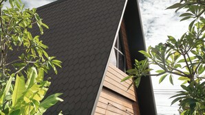 Een modern huis met een schuin dak, omgeven door weelderig groen en plantenpotten.
