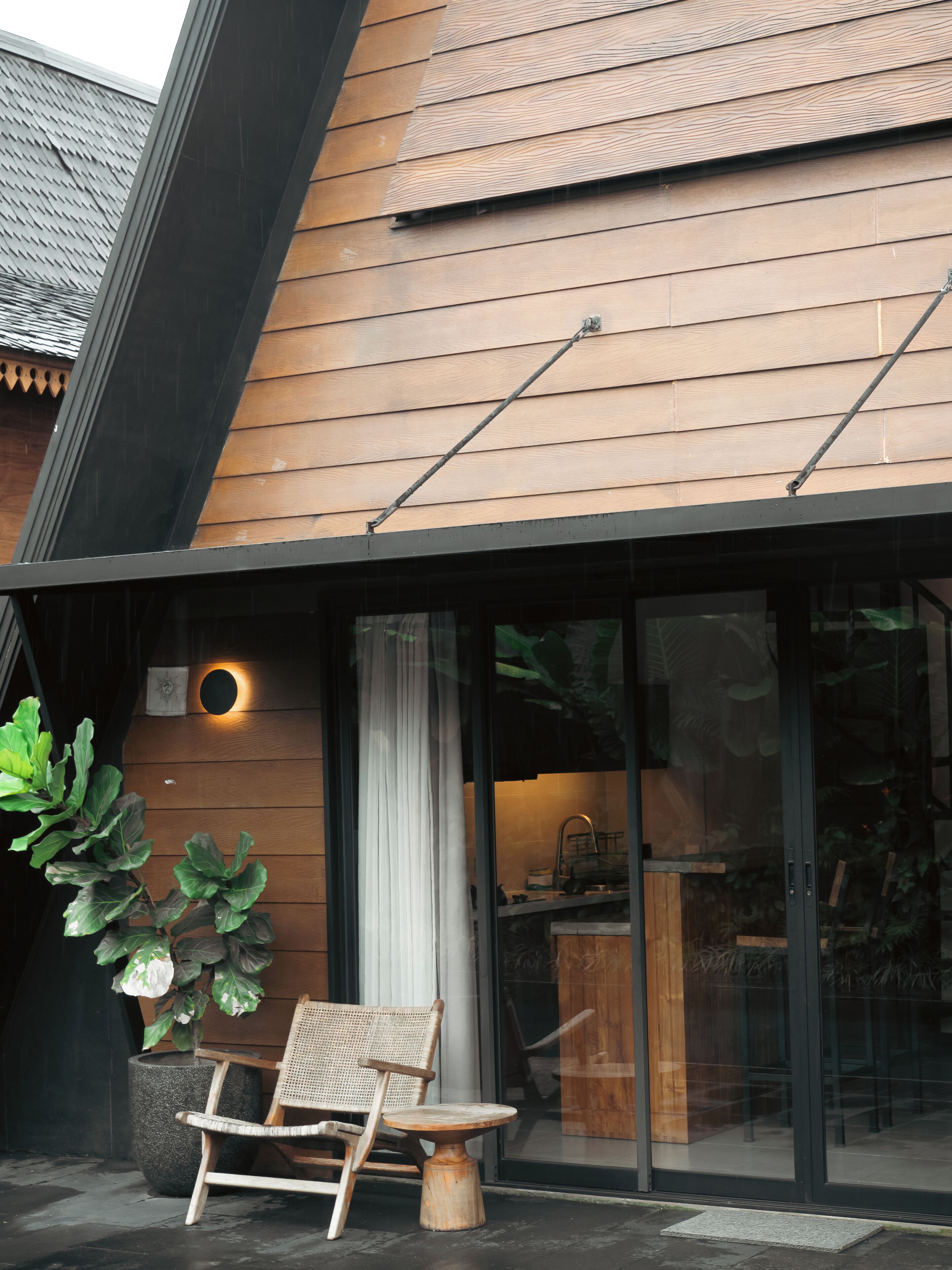 A modern building with a wooden exterior, a glass door entrance, and a seating area with a chair and table outside.