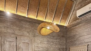 Een kamer met een rond geweven vloerkleed, een bank, een wanddecoratie van macramé en een plafondlamp.