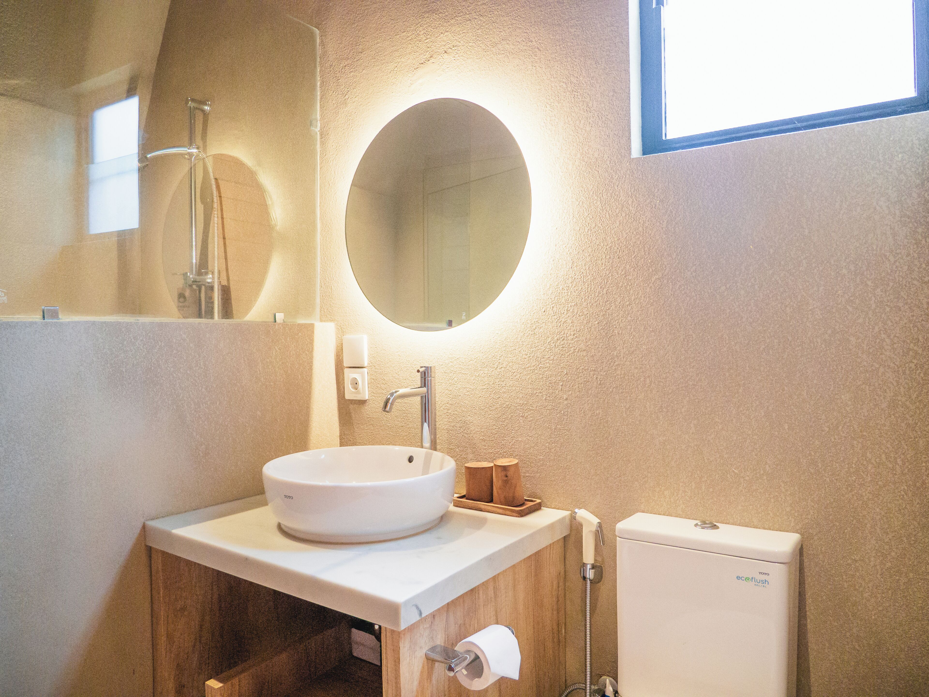 Een badkamer met een ronde spiegel, een wit wastafelmeubel, een toilet en een douche.