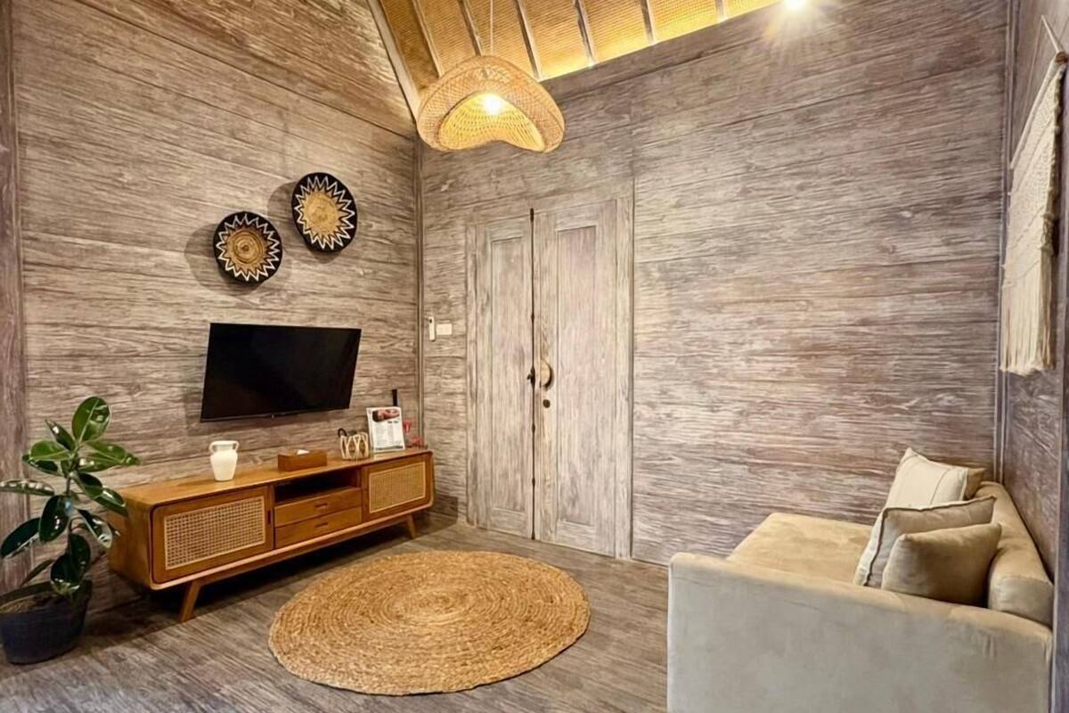 A living room with a wooden floor, a round woven rug, a sofa, a TV on a wooden cabinet, and a ceiling fan.