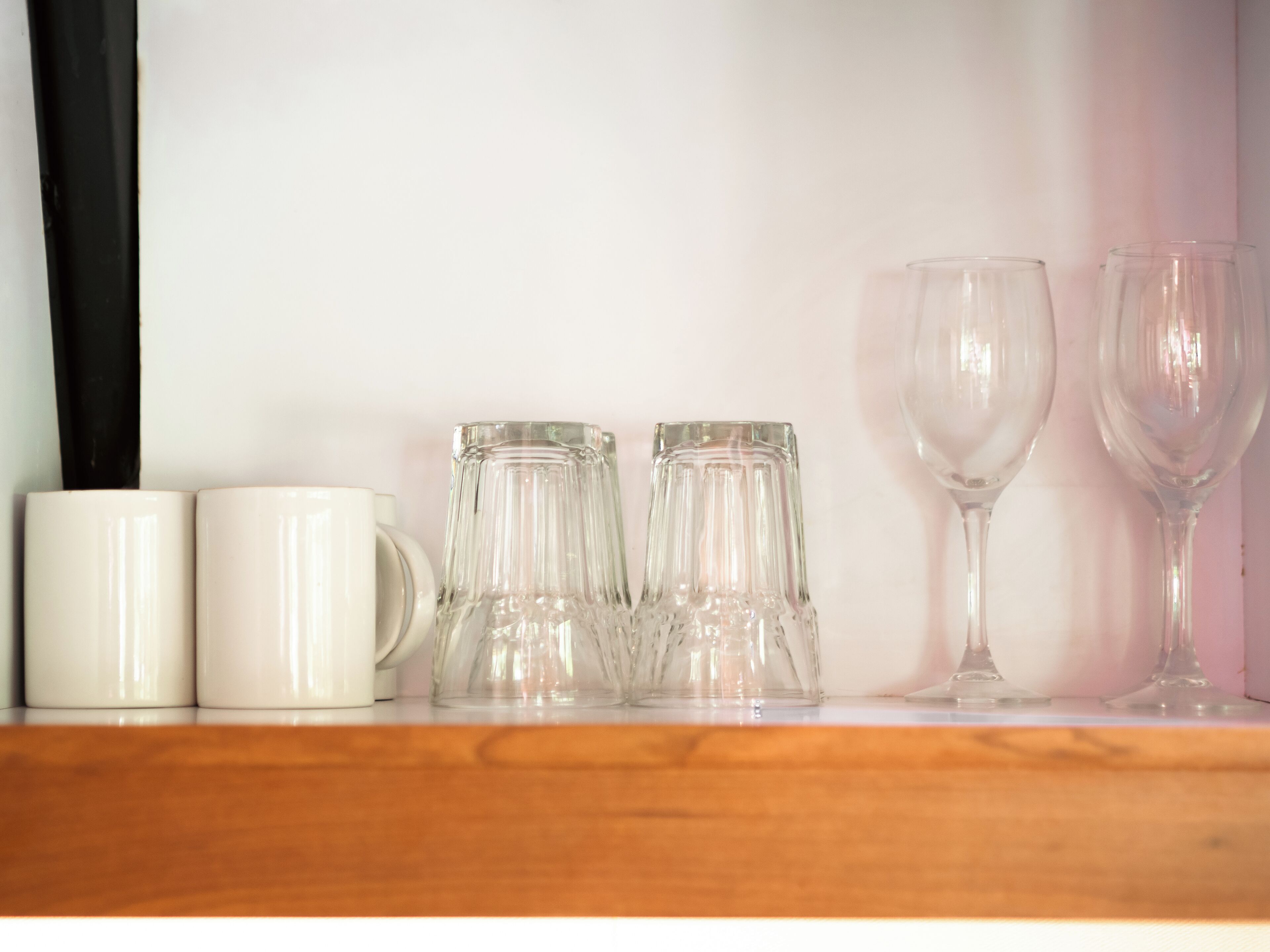 A shelf with white mugs, clear glass pitchers, and wine glasses.