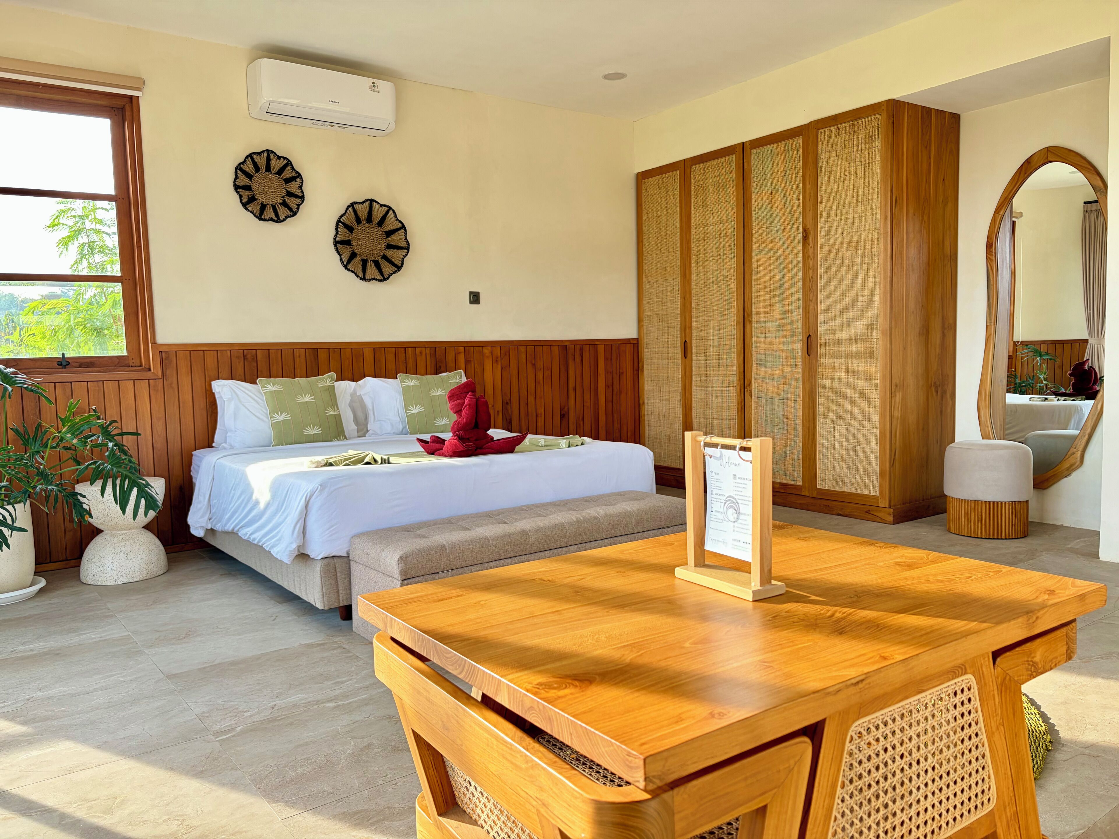 Ein Hotelzimmer mit Bett, Holztisch, Spiegel und einem großen Fenster.