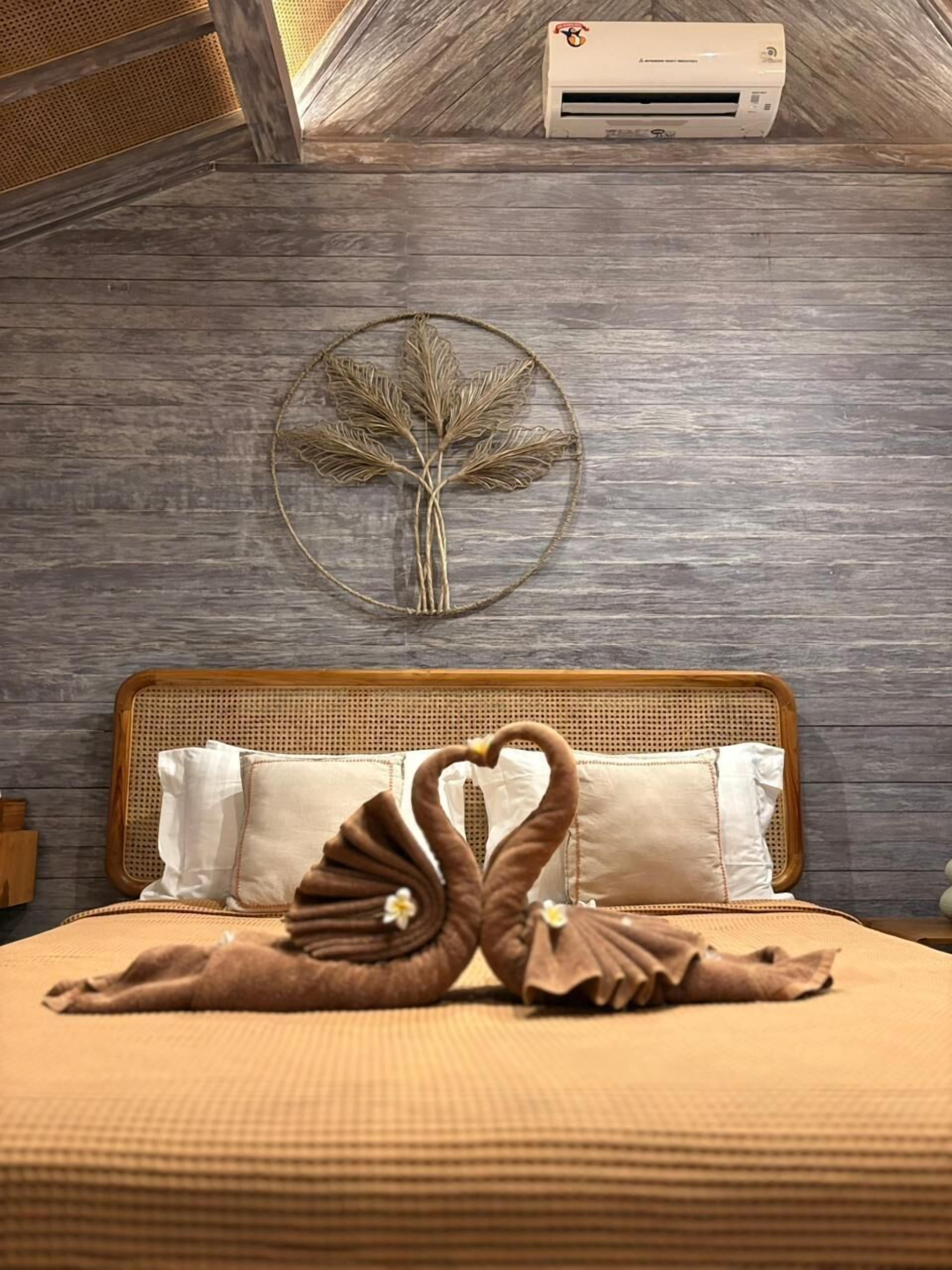 Una cama, una toalla con forma de corazón, un adorno circular en la pared y un equipo de aire acondicionado.